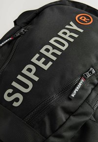 Mustmustemust mustkott mustmust mustsuure halli "SUPERDRY" logo. Omab lukke, tekstuuriga pind ja väike punane sildiga.