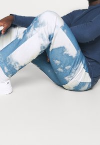 Blå och vita joggers med molnmönster i mjukt tyg, med en figursydd design och kontrasterande ränder, samt en avslappnad passform vid anklarna.