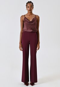 Pantalons évasés bordeaux associés à un top sans manches à col drapé dans une teinte assortie, avec de fines bretelles et une texture de tissu lisse.