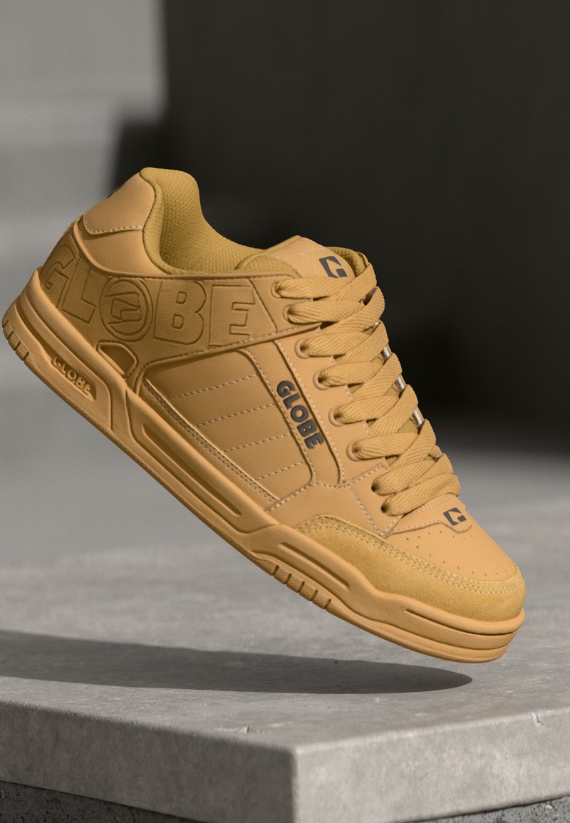 Yellow leather sneaker with padded collar, flat laces, textured surface, and "GLOBE" branding on the side. Rubber sole with grip patterns.