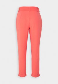 Korallfärgade byxor med en åtsittande midja, insvängda ben och upprullade fållar. Tillverkade av ett slätt tyg med minimal struktur och utan synliga detaljer.