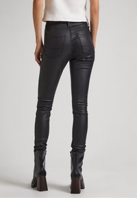 Jeans ajustados de imitación cuero negros con cintura alta, que cuentan con dos bolsillos traseros y una textura suave. Combinados con botas negras de tacón grueso.