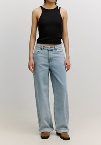 Zwart geribd crop tanktop met smalle bandjes, gedragen met lichtblauwe wijdvallende jeans met traditionele zakken en een vervaagde afwerking.