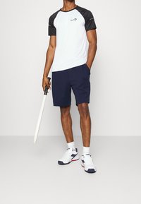 Valkoinen urheilupaita mustilla kuvioiduilla hihoilla, tummansiniset shortsit ja valkoiset lenkkarit, joissa on tummansiniset ja punaiset yksityiskohdat. Pitelee valkoista miekkaa.