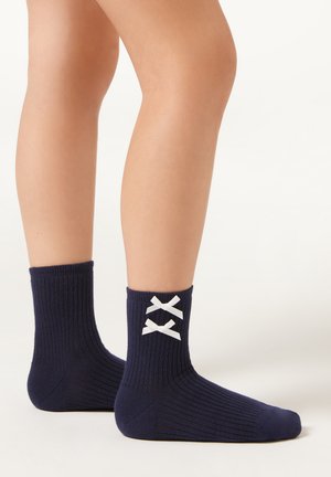 Námořnické žebrované ponožky do kotníků s texturovaným povrchem a bílými mašlemi na zadní straně. Mají přiléhavý střih a výšku do poloviny lýtka.