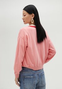 Vaaleanpunainen puuvillapaita, jossa on ribbineulottu helma ja kontrastivärinen pääntie, yhdistettynä sinisiin kuluneisiin farkkuihin.