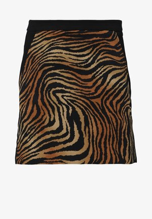 Chemise polo à imprimé zèbre brun et noir associée à une jupe noire avec une poche zippée inclinée et des baskets noires avec des accents gris.