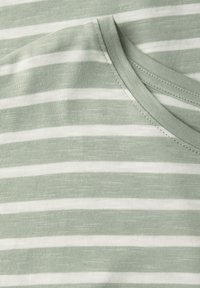 Gros plan sur un tissu rayé horizontal vert et blanc avec un encolure ronde cousue.