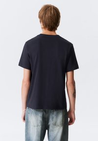 T-shirt curto de cor azul marinho escura, com decote redondo, em tecido de algodão, com um ajuste ligeiramente solto, usado com jeans de denim desgastados em azul claro.