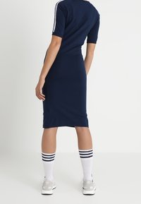 Navy bodycon dress with short sleeves, white side stripes, knee-length, paired with white socks featuring black stripes and light gray sneakers.