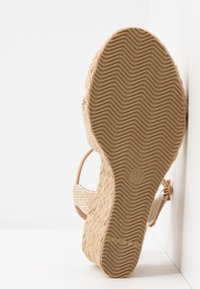 Sandale espadrille compensée avec semelle texturée, bride cheville et plateforme en jute tressé, vue par le dessous sur fond blanc.