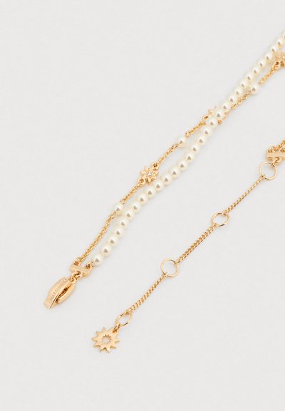 Χρυσό κολιέ επιχρυσωμένο με ασύμμετρες σειρές από λευκά μαργαριτάρια και ένα μενταγιόν σε σχήμα λουλουδιού με λεπτομέρεια από πολύτιμη πέτρα· διαθέτει κούμπωμα αστακού.