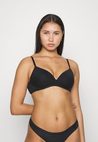 Sostenible negro sin costuras con tirantes delgados ajustables y una textura suave. Presenta una forma triangular y un diseño discreto, complementado por unas braguitas a juego.