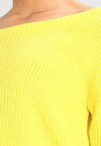 Gelber gestrickter Pullover mit einem schulterfreien Design. Verfügt über ein strukturiertes Muster und eine lockere Passform. Weicher Stoff mit geripptem Finish.