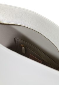 Hvid lædertaske med tekstureret overflade, der har en guldfarvet lynlås og en blød grå inderlomme med lynlåslukning.