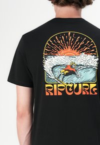 Sort bomulds t-shirt med et farverigt surfergrafik, der viser et skelet, sol og bølgedesign. "RIP CURL" tekst i orange og gule akcenter.