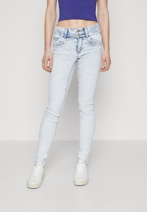 Slim fit lyseblå jeans båret med hvide sneakers og en cropped lilla top, der viser den nederste torso og ben.