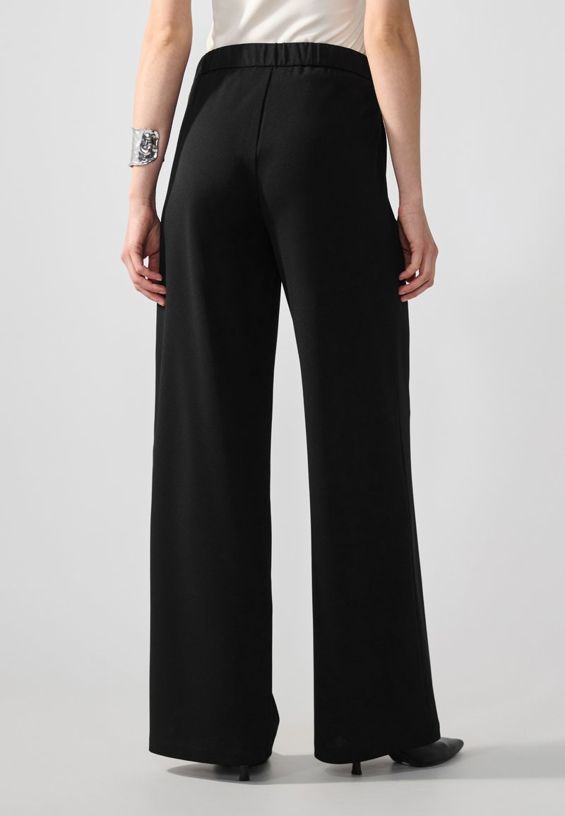Pantaloni neri a vita alta con un design a gamba larga, realizzati in un tessuto morbido. Presentano una vita elastica e un taglio stretto alla caviglia.