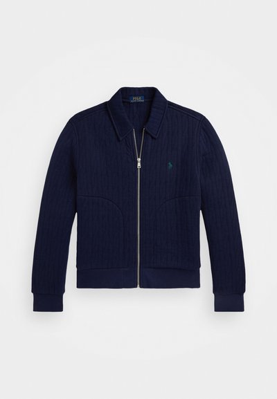 Casaco acolchoado azul marinho com colarinho, punhos e barra canelados. Apresenta um fecho zip e um logo bordado verde no peito.