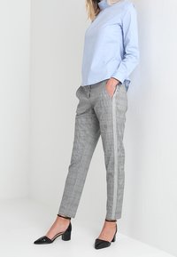 Jasnoniebieska bluzka z długim rękawem zestawiona z szarymi spodniami w kratę z bocznym paskiem; całość dopełniają czarne lakierowane szpilki.