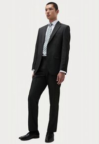 Zwart pak met een getailleerde pasvorm, bestaande uit een single-breasted jas en broek. Lichtblauwe stropdas met strepen maakt de outfit compleet.