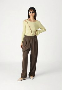 Gerippter, schulterfreier, hellgrüner Pullover mit Knopfdetails, kombiniert mit braunen, locker sitzenden Hosen mit elastischem Bund und beigen Ballerinas.