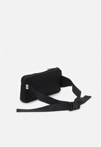 Sac à taille noir en nylon avec une forme rectangulaire, fermeture éclair et sangle réglable avec boucle en plastique. Texture lisse, design minimal.