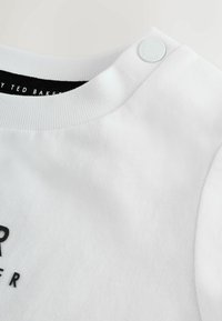 Felpa bianca in cotone con collo a costine, caratterizzata da un logo stampato nero sul davanti e un dettaglio a bottone a pressione rotondo sulla spalla.
