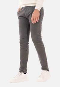 Pantaloni grigi slim-fit realizzati in materiale misto cotone, caratterizzati da una texture liscia e dettagli di cucitura sottili, abbinati a scarpe da ginnastica bianche.