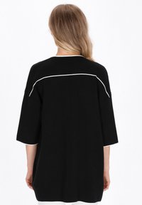 Schwarzes, übergroßes Oberteil mit einer weichen Textur, das eine weiße Akzentlinie entlang der Schulternaht und halblangen Ärmeln aufweist. Einfaches, minimalistisches Design.