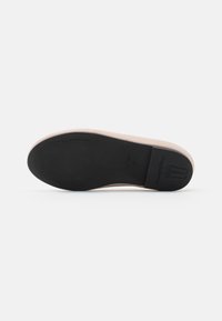 Suola piatta con una gomma nera liscia e un bordo superiore di un rosa pallido. Impronta del logo ben visibile sul tallone, design minimalista.