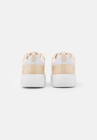Beige sneakers med vadderade baksidor, vita sulor och präglad branding. Slät material med en blank yta och minimalistisk design.