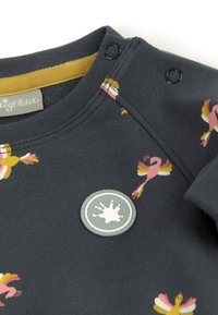 Sweatshirt gris foncé avec des motifs de flamants colorés, des accents de col jaune et des fermetures à pression décoratives. Texture en coton douce.