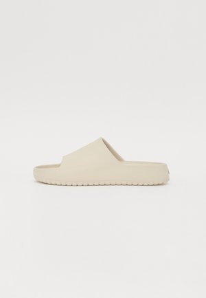 Beige színű csúszó szandál sima felülettel, nyitott orral és széles pánttal. A textúrázott talp biztosítja a tapadást. Egyszerű, minimalista dizájn.