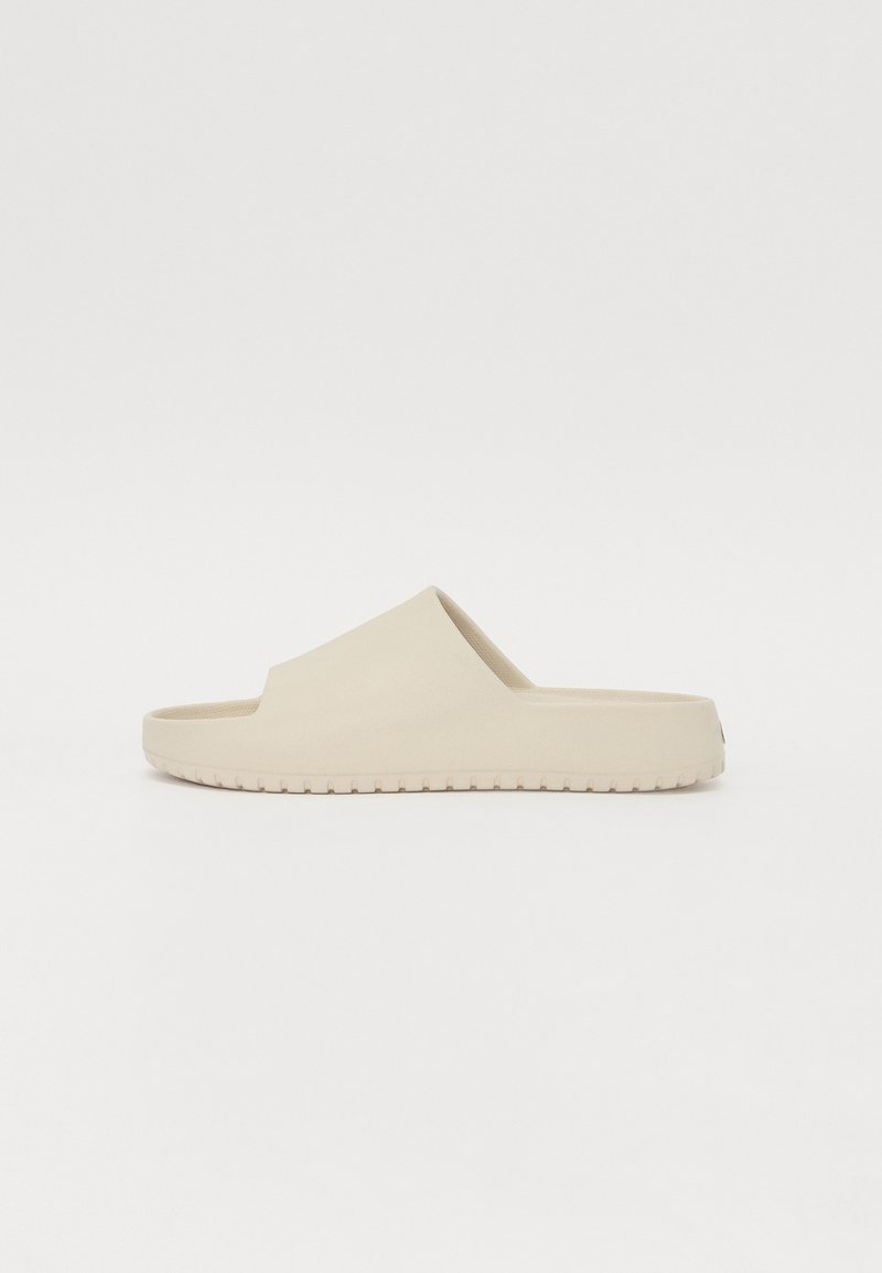 Beige slide sandal with a smooth finish, open toe, and a wide strap. Textured sole provides grip. Simple, minimalistic design.