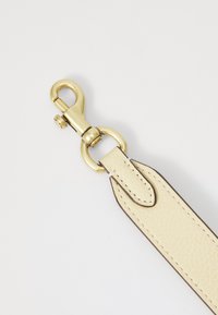 Leather bag strap in cream with a textured surface and brown edging, featuring a gold metal clip and circular hardware attachment.