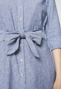 Robe rayée bleue et blanche avec des boutons sur le devant et une ceinture nouée en nœud à la taille, avec des manches trois-quarts.