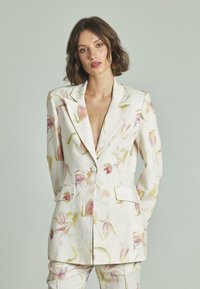 Blazer blanco de lino con patrones florales rosados, solapas con muesca, cierre de un solo botón y dos bolsillos frontales. Ajuste entallado que realza la estructura.