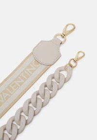 Beige justerbart band med kedjedesign, som har en slät yta och guldhardware. Inkluderar en fusk läderfäste med logotyp.