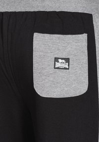 Svarta bomullsjoggers med en grå ficka och en svart etikett som läser "LONSDALE LONDON." Mjuk textur med elastisk midja.