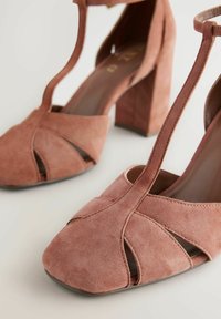 Talons en daim rose poussiéreux, avec un bout ouvert et un design de découpes entrecroisées. Le talon carré apporte de la stabilité. Finition intérieure lisse.
