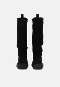 Bottes montantes en daim noir avec une semelle en caoutchouc texturée, dotées d'une fermeture éclair latérale et de languettes en haut pour faciliter l'enfilage.