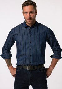 Mørk denim skjorte med knapper og lodrette striber, lange ærmer der er rullet op ved manchetterne, enkelt brystlomme og sorte knapper. Kombineret med mørke jeans og bælte.