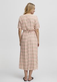 Robe imprimée florale, longue jusqu'à la cheville, avec des manches courtes, taille cintrée et un tissu léger dans des couleurs pastel de rose, vert et crème.