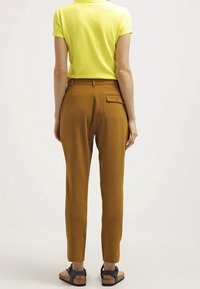 Gul polo-tröja, bruna tapered byxor med bakficka och svarta sandaler. Slät tyg och skräddarsydd passform med en modern silhuett.