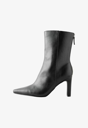 Zwarte leren enkellaars met een spitse neus, hoge hak en een rits aan de achterkant. Gladde textuur met minimale stikseldetails.
