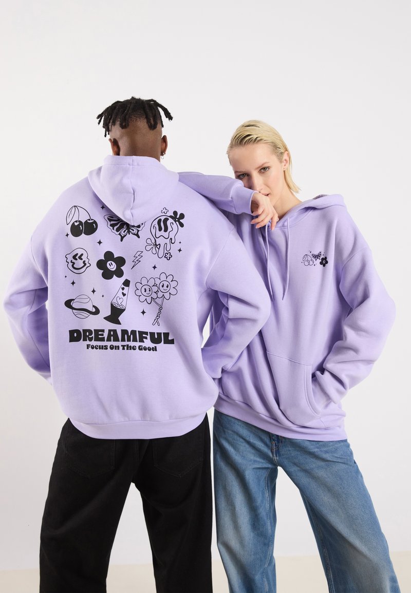 Sweat à capuche lilas avec des motifs graphiques noirs, incluant des fleurs de style cartoon, des cerises et le texte "DREAMFUL Concentre-toi sur le positif."