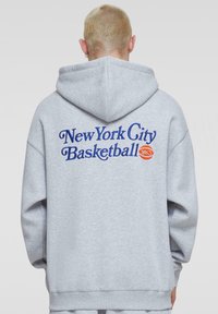 Grå hætte sweatshirt med blå broderet tekst "New York City Basketball" samt et basketball grafik, løstsiddende pasform og elastiske manchetter.