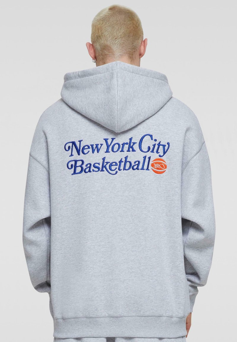 Grå hætte sweatshirt med blå broderet tekst "New York City Basketball" samt et basketball grafik, løstsiddende pasform og elastiske manchetter.