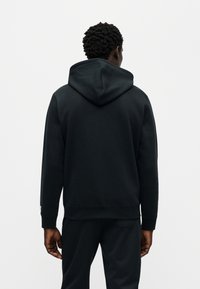 Μαύρο φούτερ με κουκούλα και χαλαρή εφαρμογή, διαθέτει αδιάκοπο σχεδιασμό στην πλάτη, ριμπ μανσέτες και απαλό ύφασμα. Διακριτικό λογότυπο στο μανίκι.